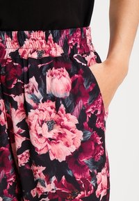 Rekbare zwarte stoffen shorts met een bloemenpatroon met grote roze pioenen en subtiele bladeren. Elastische tailleband en zijzakdetails.