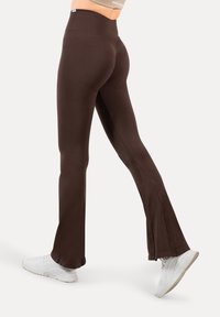 Brune viddeleggings lavet af strækbart stof med høj talje og glat tekstur, kombineret med hvide sportssko.