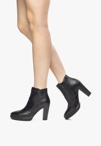 Bottines en cuir noir avec un talon bloc haut, dotées d'une fermeture éclair latérale et de clous décoratifs sur le col pour un détail supplémentaire.