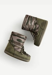 Bottes à motif camouflage avec une tige rembourrée dans des nuances de vert et de marron, dotées d'un matériau doux et texturé ainsi que de fermetures à lacets.