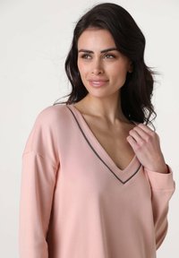 Blusa a maniche lunghe color rosa chiaro con scollo a V e bordo grigio a contrasto. Tessuto morbido, vestibilità rilassata, con spalle scese e texture liscia.