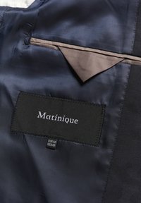 Tejido de satén negro con un forro interior gris claro; cuenta con una etiqueta cosida "Matinique" y etiquetas de talla, mostrando una textura suave y un diseño elegante.