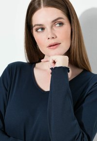 Maglietta a manica lunga blu navy con texture a coste, caratterizzata da un collo rotondo e bordi sfilacciati sui polsini delle maniche.