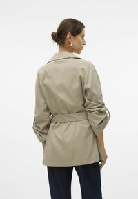 Chaqueta beige ligera con cintura ceñida, corte relajado, mangas enrolladas y cuello con muesca, con una textura suave.