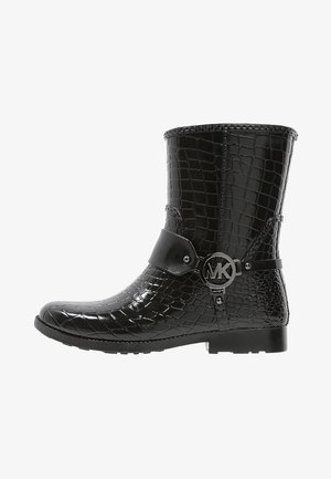 Stivaletto nero lucido alla caviglia con una texture a coccodrillo, punta rotonda e una cinghia con un accento di logo circolare, dotato di una suola piatta in gomma.