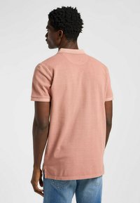 Kortärmad piké i dammig rosenfärg, tillverkad av texturerad tyg med krage, sida sprund och en avslappnad passform.