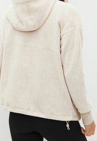 Sudadera de forro polar en un beige claro con un ajuste holgado, que cuenta con una capucha forrada, puños acanalados y un dobladillo ajustable con cordón para modificar la longitud.