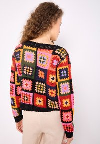 Strickjacke im Granny-Square-Design mit mehrfarbigen Mustern in Rot, Pink, Grün und Schwarz, mit einem gerippten schwarzen Kragen und Saum.
