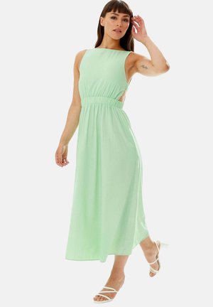 Light green, sleeveless maxi dress with a fitted bodice, side cutouts, and an elastic waist. Smooth fabric with a subtle texture. White strappy sandals.
