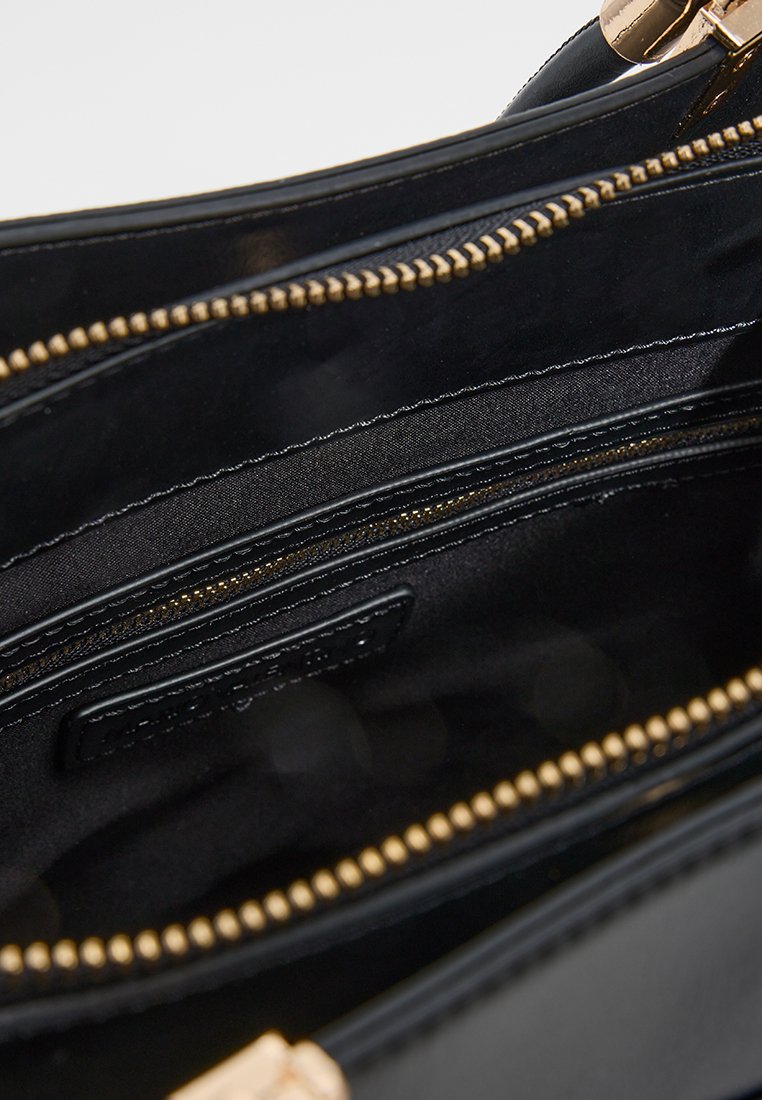 Interno di una borsa in pelle nera con numerosi scomparti con zip, accessori in oro e una texture liscia. Etichetta visibile all'interno.