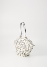Bolso tote blanco con intrincado patrón floral en corte, borde superior con ondas, herrajes en tono dorado y asas dobles de cuero negro.