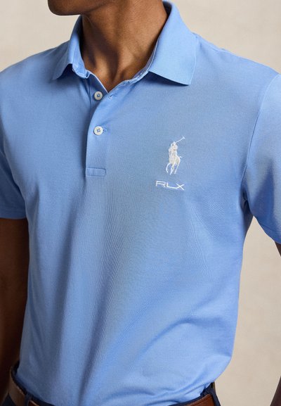 Uomo che indossa una polo azzurro chiaro con un logo ricamato bianco del giocatore di polo e testo "RLX" sul petto.