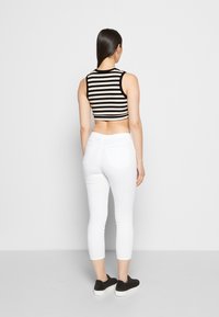 Top corto a righe bianche e nere, pantaloni bianchi aderenti e sneakers nere. Vista dal retro, evidenziando la forma e la vestibilità.