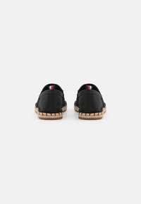 Paire de chaussures espadrilles noires à enfiler avec semelles en fibres naturelles tissées, vues de dos sur fond blanc.
