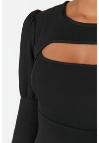 Svart topp med puffärmar och en rektangulär utskärning vid bröstet. Tillverkad av ett slätt tyg, med sömnadsdetaljer längs kanterna.