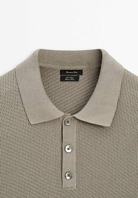 Beige neulottu poolopaita, jossa on resorikaulus, kolme hopeista nappia ja teksturoitu kuvio. Etiketissä lukee "Massimo Dutti."