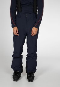 Marineblauwe skibroeken met elastische bretels, knoopsluiting en brede pijpen, voorzien van een gladde textuur en versterkte stiksels bij de zakken.