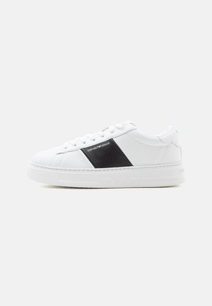 Valge madala säärega toss, musta külgpaneeli ja Emporio Armani logoga, valgete paelte ja paksu valge tallaga lihtsal taustal.