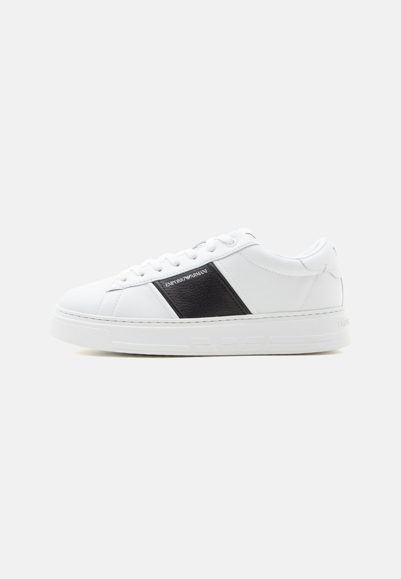 Baskets basses blanches avec panneau latéral noir et logo Emporio Armani, lacets blancs et semelle blanche épaisse sur fond uni.