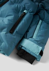 Teal pufferjakke med svarte mansjetter, med to glidelåslommer og kontrasterende stoffdetaljer. Glatt, quiltet tekstur med slitesterke materialer.