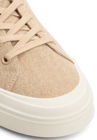 Beige canvas sneakers med texturerad yta, rund tå och vit gummisula. Har beige snören och metallöglor för fastsättning.