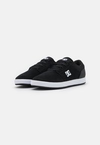 Scarpe da skate in suede nero con suole in gomma bianca, dotate di lacci rotondi e un logo sul lato. Design minimalista con una finitura testurizzata.