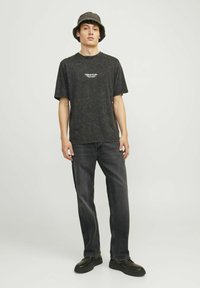 Svartprickig t-shirt med korta ärmar, i kombination med mörka jeans. Modellen bär en grön bucket hat och svarta klumpiga skor.