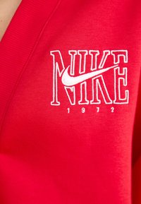 Röd sweatshirt med vit broderad "NIKE"-logga och swoosh, med "1972" under. Mjukt tyg och ribbad nacklinjetextur.