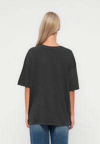Donkergrijze katoenen t-shirt met korte mouwen, ronde hals, verlaagde schouders en een relaxte pasvorm. De achterkant toont een gladde textuur en eenvoudig ontwerp.
