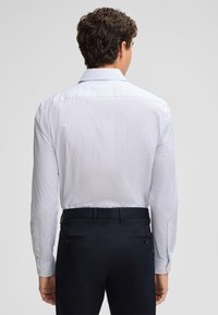Witte longsleeve shirt met een klein marineblauw stippenpatroon, voorzien van een eenvoudige kraag en knoopmanchetten, gecombineerd met donkere broek.