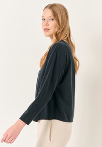 Maglietta a maniche lunghe grigio scuro con vestibilità comoda, tessuto morbido, scollatura rotonda e spacchi sui lati, mostrata su un modello di profilo.