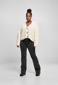 Off-white, stickad cardigan med V-ringning, oversize design och stora knappar, matchad med svarta vida jeans och svarta skor.