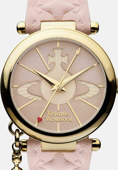 Horloge met een roze leren band, goudkleurige hardware, ronde wijzerplaat, gestructureerde wijzerplaat, gouden uurmarkeringen en een klein rood hartaccent.