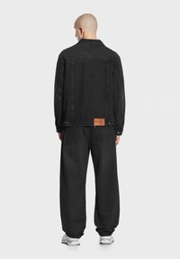 Czarna dżinsowa kurtka o luźnym kroju i zapięciu na guziki, w połączeniu z luźnymi czarnymi dżinsami. Posiada brązową skórzaną metkę z tyłu.