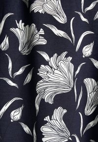 Tissu bleu marine arborant des motifs floraux blancs avec des détails de lignes complexes et des motifs de feuilles fluides. Texture douce, matière de poids moyen.