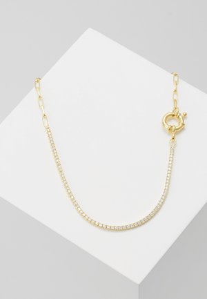 Collier chaîne en or avec une rangée de petites pierres claires et un fermoir circulaire, présenté sur une surface blanche inclinée.