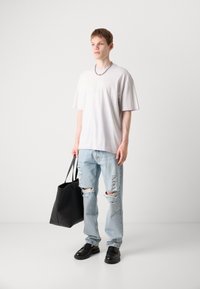 Lys grå oversized t-shirt med præget tekst, slidte lyseblå jeans, sorte lædersko og en sort totebag.