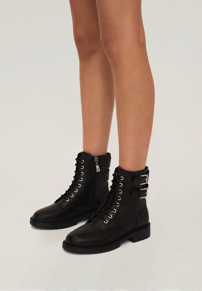 Black leather ankle boots with lace-up front, side zipper, buckle accents, and textured sole. Features silver eyelets and a round toe shape.
