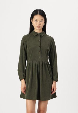 Robe en velours côtelé vert avec un col chemise, un devant à boutons, des manches longues, une taille froncée et une longueur au genou. Présente une texture à côtes verticales.