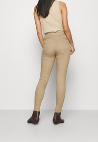 Beiga högmidjade leggings gjorda av ett slätt stretchmaterial, med bakfickor och en tight passform. Avslutade med bruna ankelstövlar.