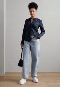 Námořnická košile na knoflíky, světle modré vysoké široké džíny, bílé platformové tenisky a malá černá kabelka. Hladké textury po celém outfitu.