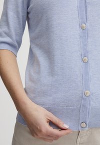 Lichtblauwe cardigan van zacht materiaal, met een geribde zoom en drie glanzende decoratieve knopen aan de voorkant.