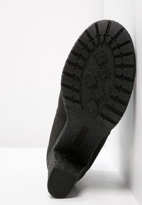 Semelle de botte noire en caoutchouc texturé, dotée d'un motif de bande de roulement avec plusieurs grips pour une adhérence optimale et une forme angulaire vers le talon.