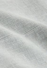 Textil gris claro con un patrón tejido que presenta una textura sutil y líneas finas distintivas. Acabado suave, brillo mínimo y caída suave.