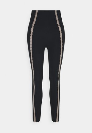 Leggings noirs à taille haute avec des bandes latérales beige festonnées. Fabriqués en matière extensible, design ajusté et coupe à la cheville.