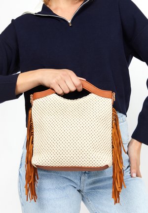Vævet beige håndtaske med brune læderdetaljer, der har frynseelementer og et rundt topgreb. Den teksturerede overflade tilføjer visuel interesse.