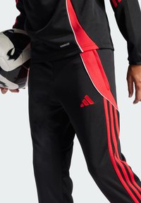 Sorteidrettsjakke med svart bukse som har røde side-striper og et brodert logo. Glatt tekstur med en slim fit. Holder en svart og hvit fotball.