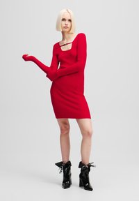Rochie roșie cu dungi, cu mâneci lungi și decolteu pătrat, având o mică embellisment la piept. Purtați cu cizme negre strălucitoare până la gleznă.