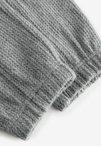 Tissu en tricot gris présentant un design texturé et à côtes. Le matériau a l'air doux, avec des poignets élastiqués mettant en valeur un motif de couture détaillé.