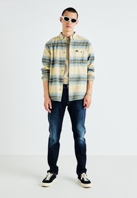 Vaaleanbeige ja siniraitainen nappipaita, vaaleanbeige t-paita alla, tummat farkut, mustat lenkkarit ja valkoiset aurinkolasit.